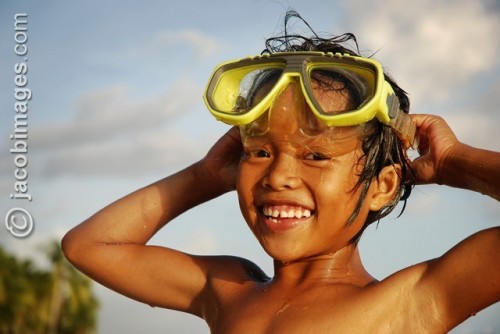 A local girl swimming with goggles smiles in the late evening sun 